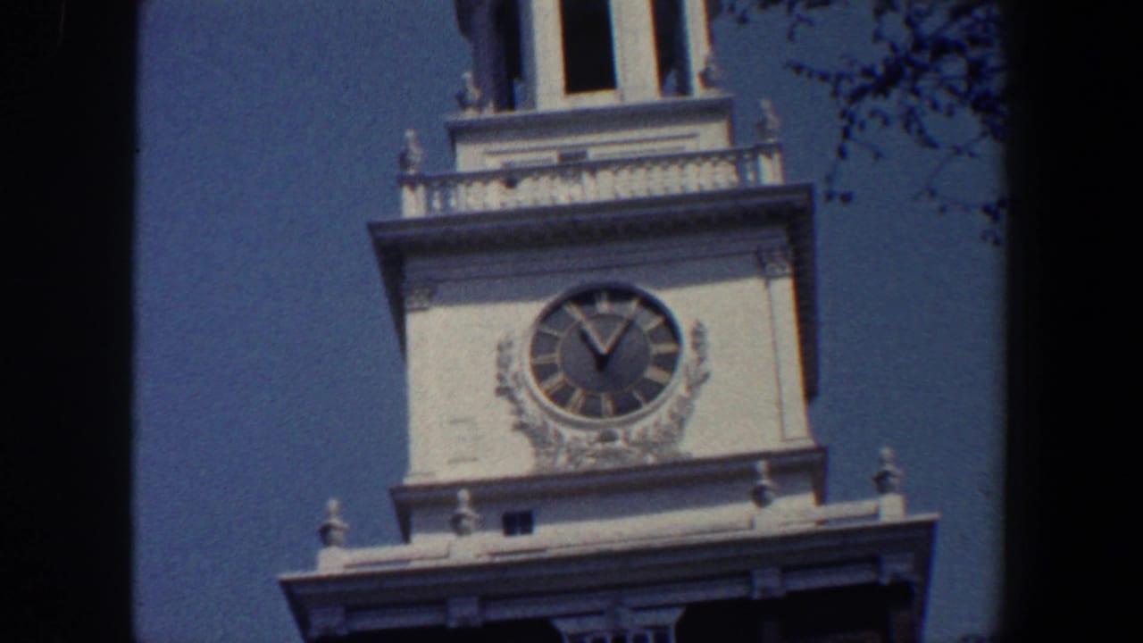 White clock tower with Roman-numeral clock face against blue sky.