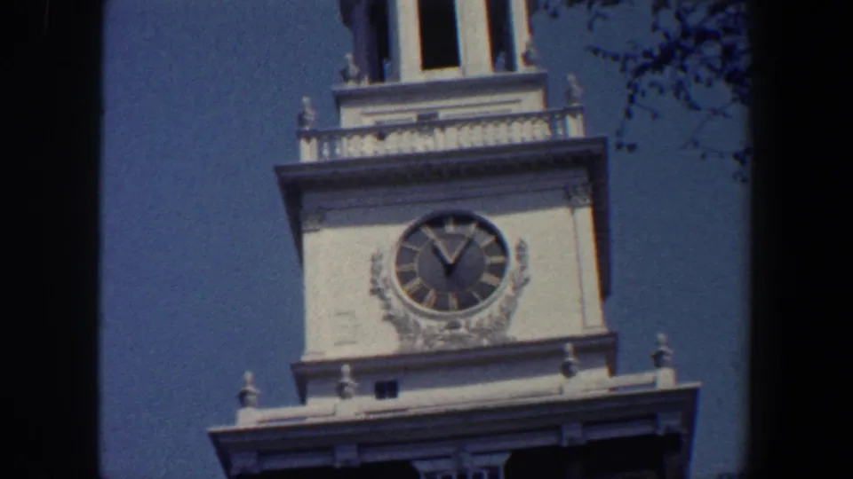 1962 Philadelphia home-movie frame showing a white clock tower and Roman-numeral clock face above a darker facade.
