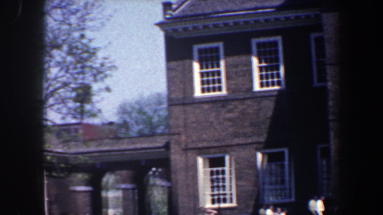 Brick building wing with tall windows, connecting archway, trees, and small pedestrians.