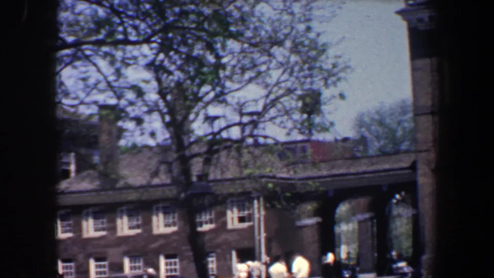 1962 Philadelphia home-movie view of a lower brick range, arched passage, bare tree branches, and pedestrians in the foreground.