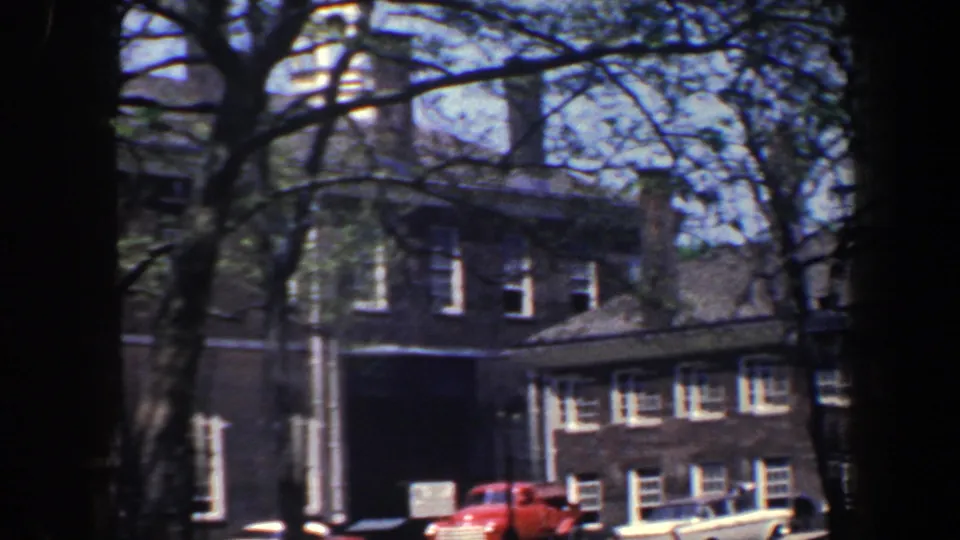 1962 Philadelphia frame showing brick architecture, an archway, tree branches, and parked cars along the street.