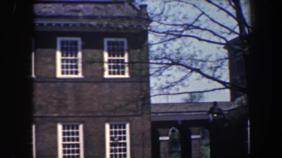 1962 Philadelphia view of a brick building corner with white windows, tree branches, and a distant arched or covered structure.