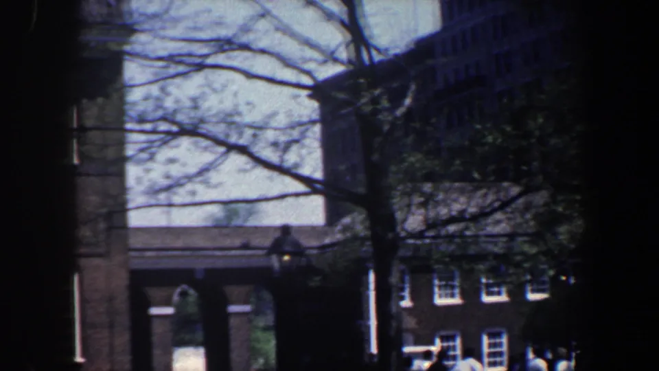 Philadelphia street scene from 1962 with branches, a brick building edge, a street lamp, and distant windows in soft 8mm color.