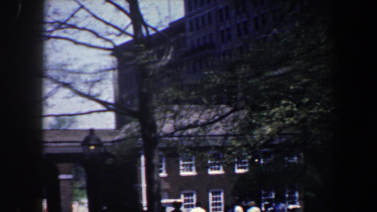 1962 Philadelphia home-movie view through trees toward brick buildings with white-trimmed windows and shaded street frontage.