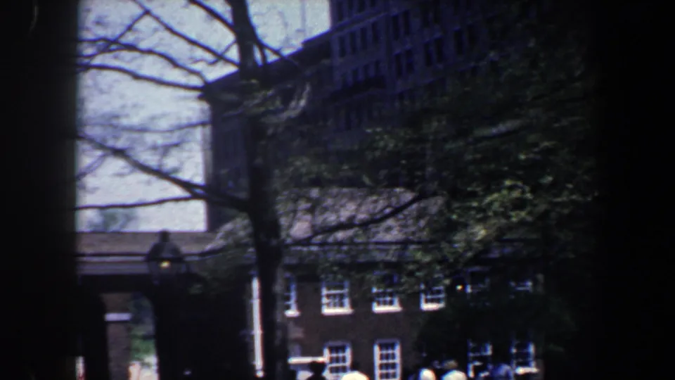 1962 Philadelphia home-movie view through trees toward brick buildings with white-trimmed windows and shaded street frontage.