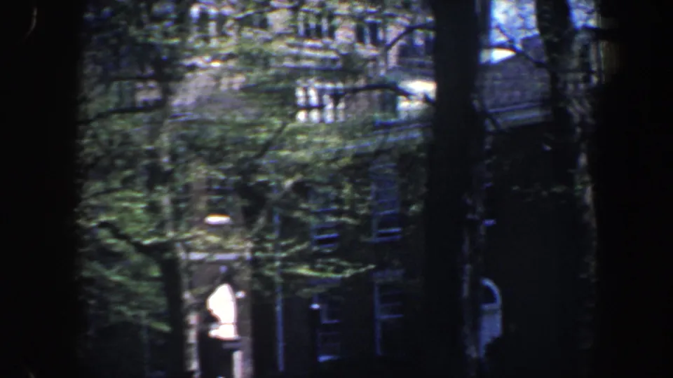 1962 Philadelphia home-movie frame showing a brick building with arched entry details, windows, trees, and bright foliage.