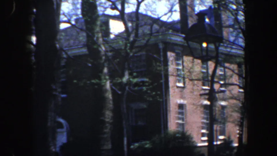 1962 Philadelphia exterior with a brick corner facade, white-trimmed windows, tree branches, and a street lamp in view.