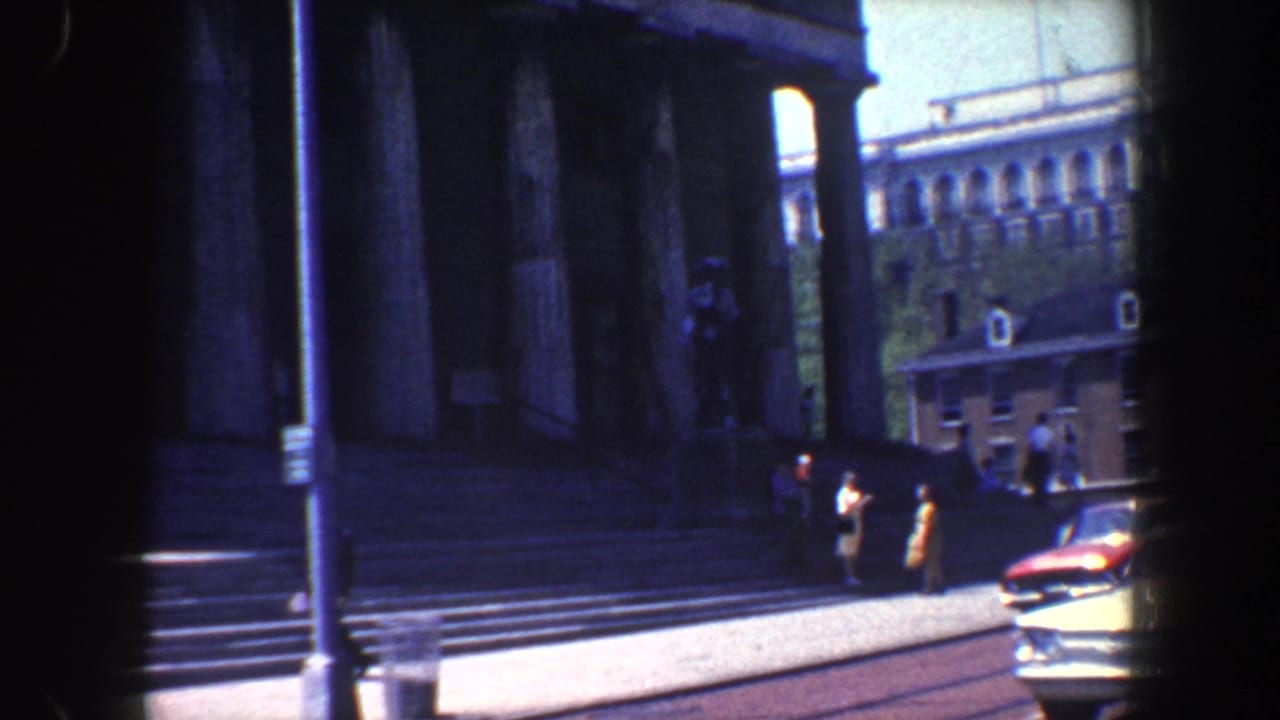 1962 Philadelphia street-level view of a large classical building with columns, steps, pedestrians, and a period car nearby.