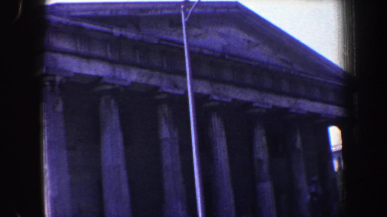 1962 Philadelphia home-movie frame showing a columned neoclassical facade, triangular pediment, and tall streetlamp in soft 8mm color.