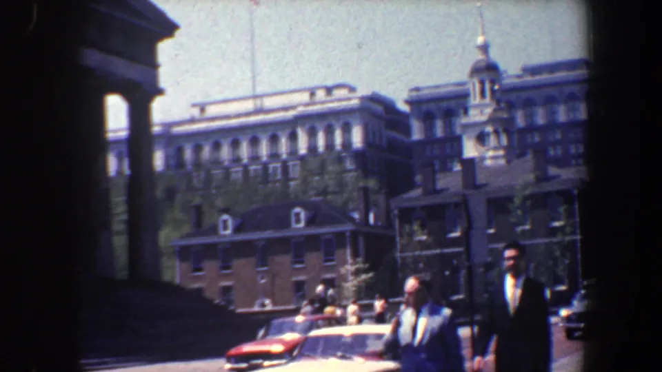1962 Philadelphia home-movie frame showing suited men walking near cars by the Carpenters' Hall area.