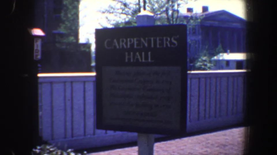 Handheld 8mm frame of the Carpenters' Hall sign in Philadelphia with courtyard fencing and gateposts.