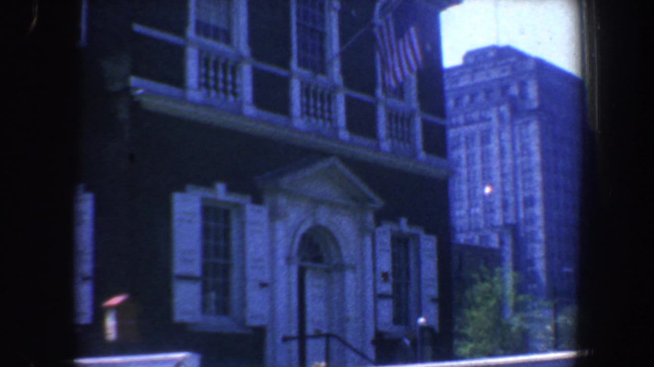 Building entrance with white shutters, arched doorway, steps, and tall city building in the background.