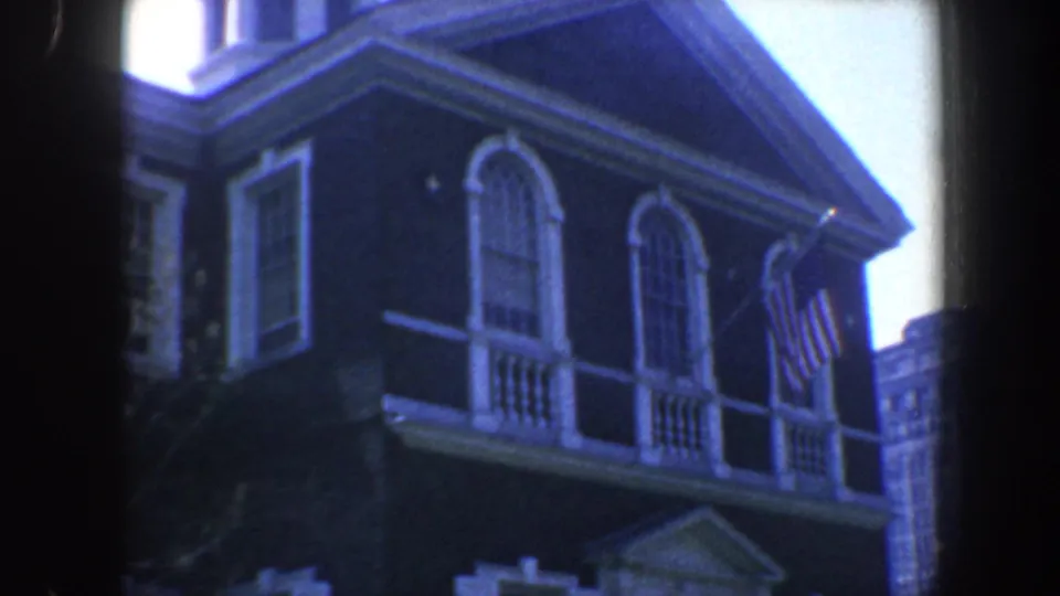 1962 Philadelphia frame of the building's upper facade, showing arched windows, white shutters, flag, roofline, and a modern tower at right.