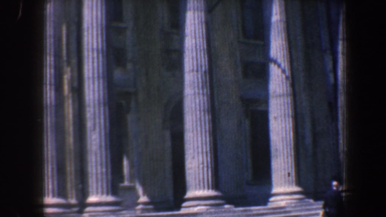 Neoclassical stone facade with tall fluted columns, steps, and a small figure near the entrance.