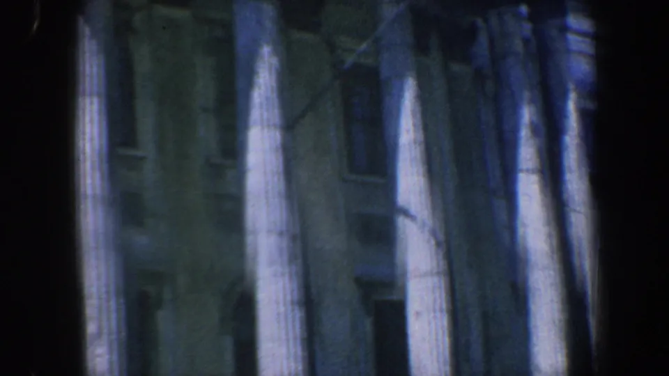 1962 Philadelphia frame showing neoclassical columns and shadowed windows, framed by dark edges from the 8mm film scan.