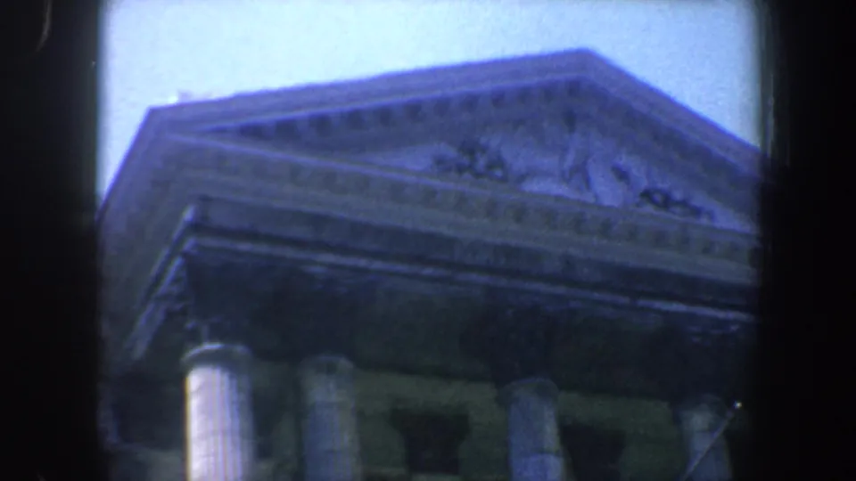 1962 Philadelphia frame looking up at a classical triangular pediment and column capitals under a pale sky.