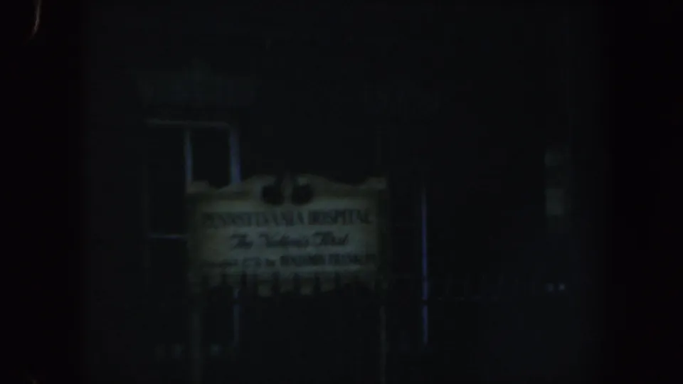 Night 8mm frame in Philadelphia showing the Pennsylvania Hospital sign against a dark building facade and nearby windows.