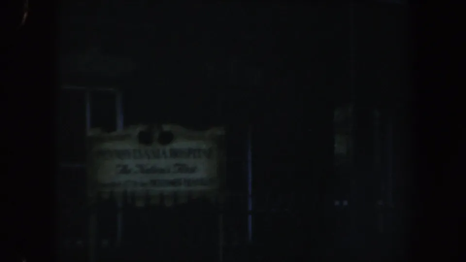 Final low-light 8mm frame of the Pennsylvania Hospital sign with a shadowed facade and window behind it.