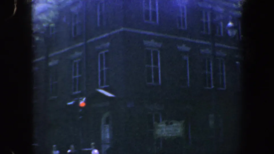 A closer 1962 Philadelphia view shows the brick building's window rows, a red traffic light, and distant sidewalk pedestrians.