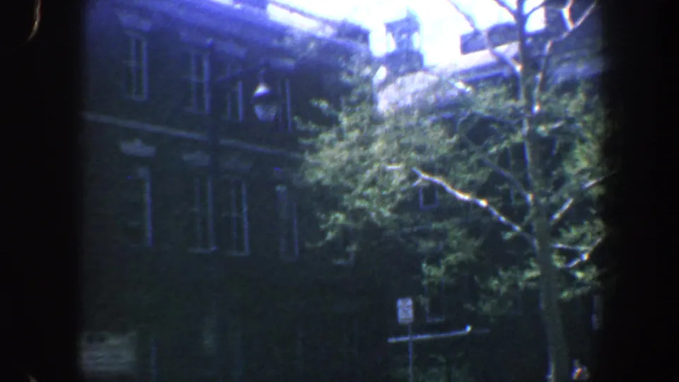 Late in the pan, leafy trees partially cover the Philadelphia brick building, with a street sign and sidewalk details below.