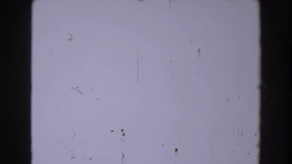 1962 North Hollywood 8mm frame area showing a pale blank field, black gate edges, dust, scratches, and visible film grain.