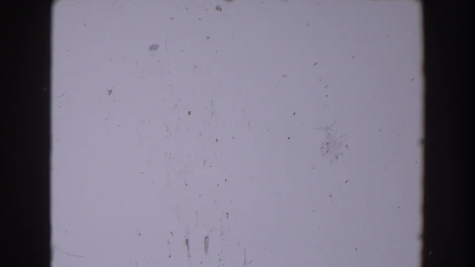 Pale 8mm film frame from the supplied 1962 North Hollywood reel, with black side borders, dust flecks, scratches, and grain.