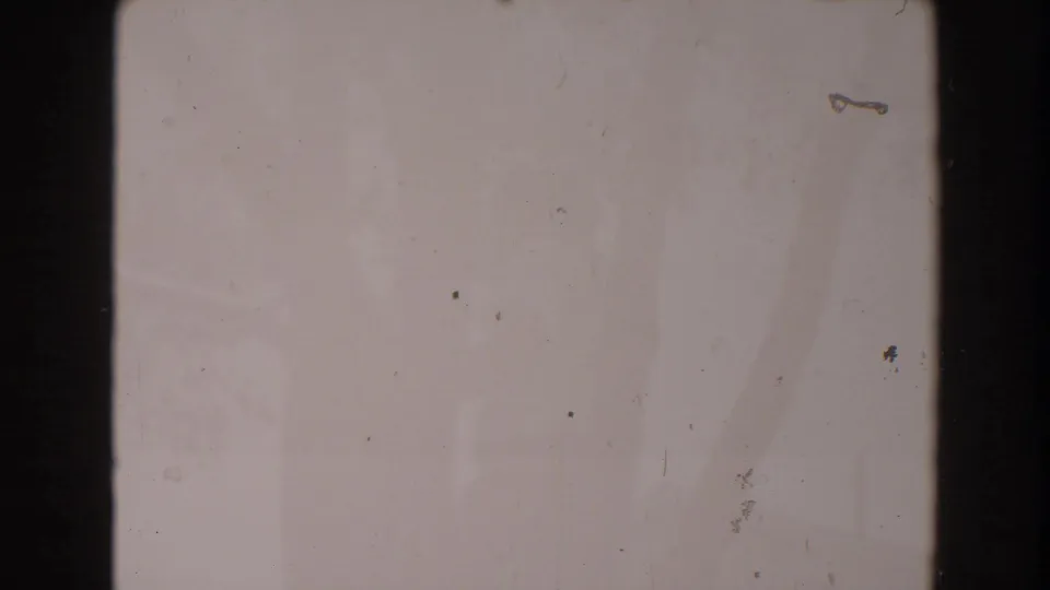 Blank 1962 8mm film frame with pale emulsion tone, dark edge, scattered debris, surface marks, and slight discoloration.