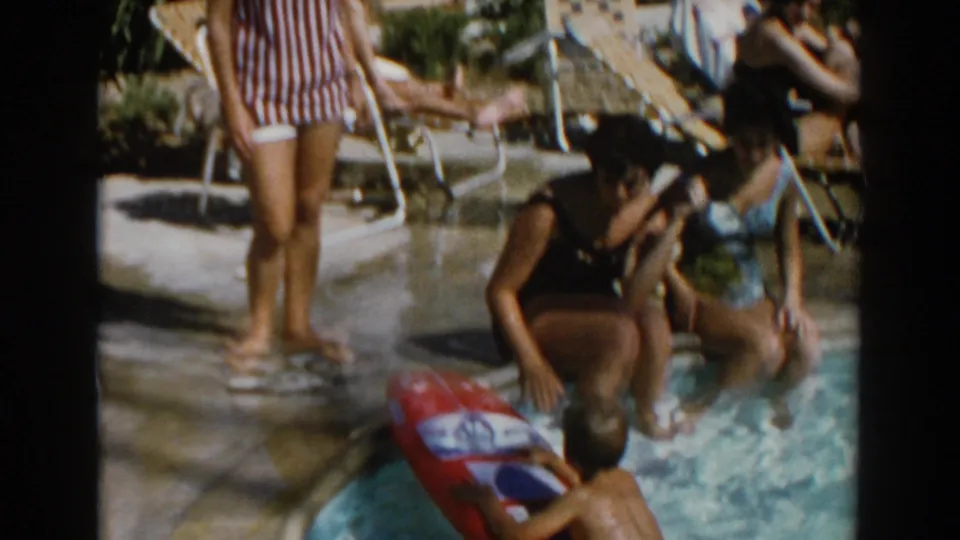 A backyard pool scene in 1962 North Hollywood shows a woman standing while other adults sit at the pool edge.