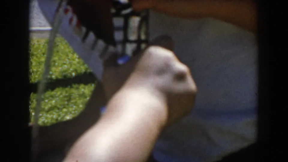 Close 1962 North Hollywood 8mm view of a forearm and hand holding a drinking fountain nozzle beside a white shirt and lawn.