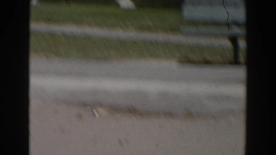 Handheld 8mm frame of North Hollywood street pavement, curb, lawn, and a small partial figure near the background.