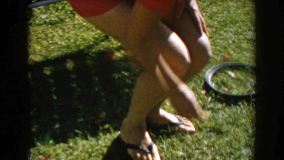 A cropped handheld frame shows the woman's legs and sandals as she steps across a grassy lawn in the yard.