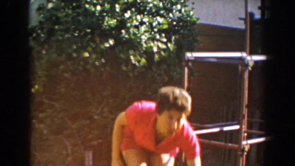 The woman bends down near the metal frame, partly blurred by motion, in 1962 backyard home-movie footage from North Hollywood.