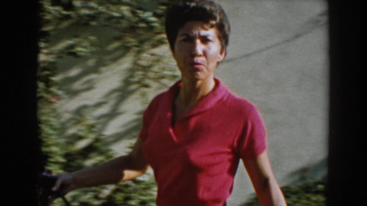Woman in a pink shirt looks toward the camera while holding a hose outdoors.