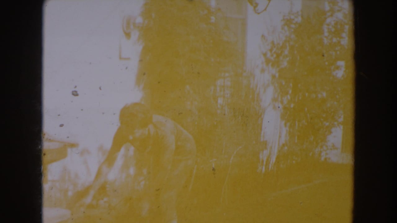 Overexposed frame of the woman bending near yard equipment, with trees and wall shapes behind her.