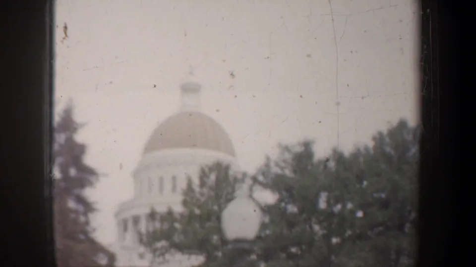 Soft 1957 California home-movie view of a domed civic building, possibly the California State Capitol, partly obscured by trees.