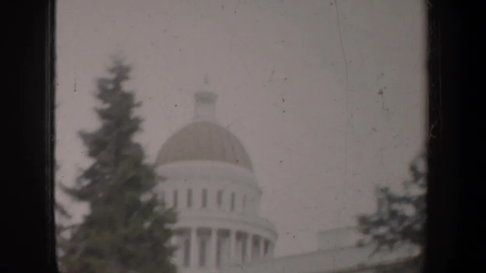 1957 8mm frame showing a domed public building behind evergreen trees, with muted color and home-movie softness.