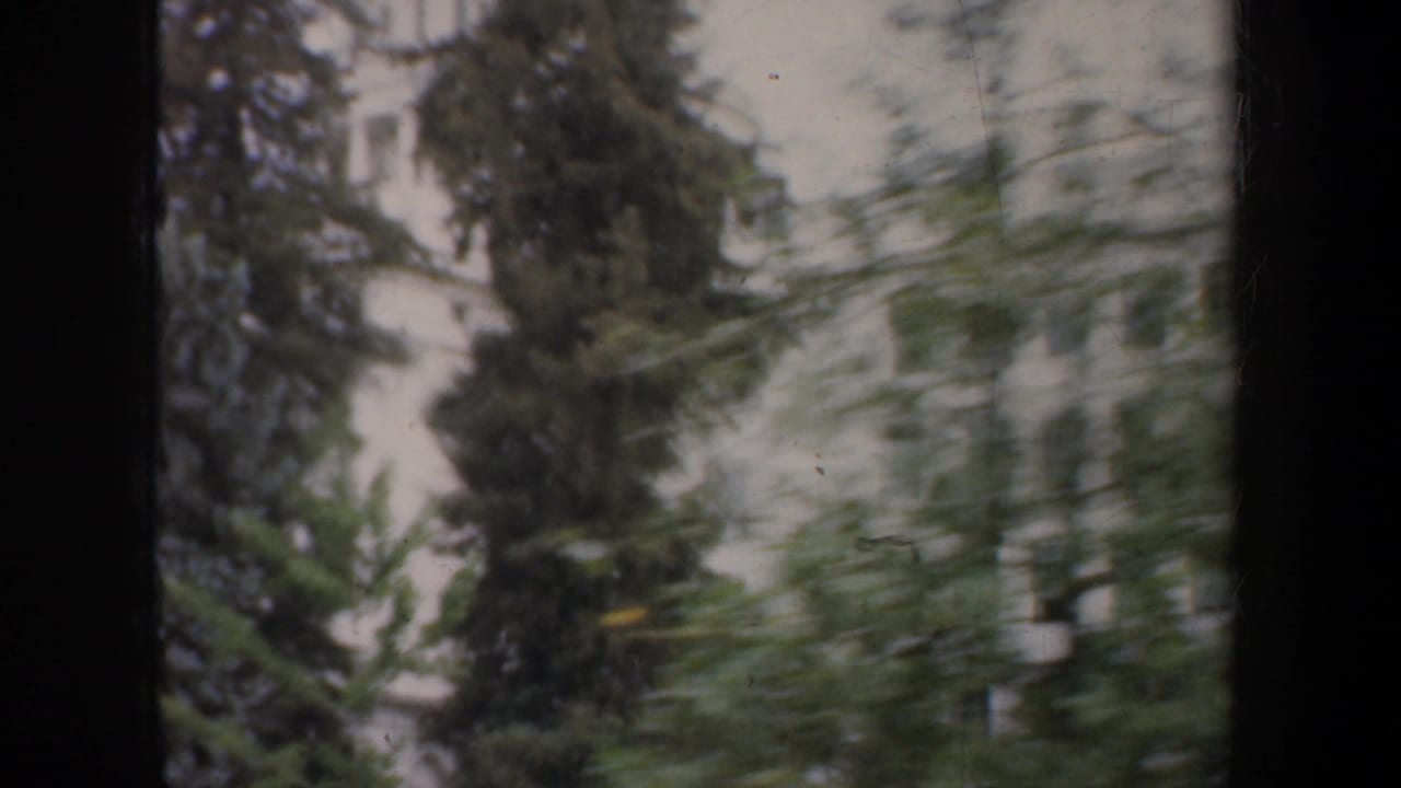 1957 San Francisco 8mm frame showing a pale urban building and trees passing in soft motion blur from a vehicle window.