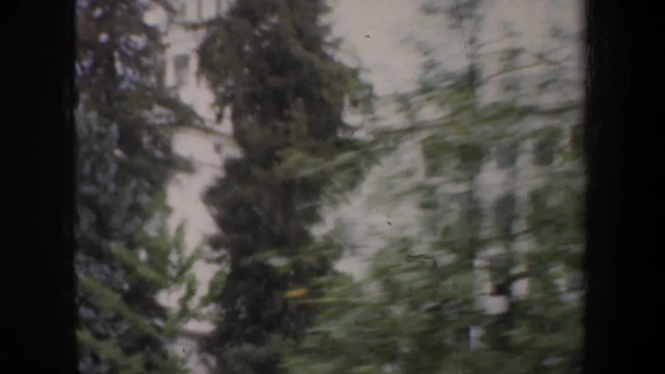 1957 San Francisco 8mm frame showing a pale urban building and trees passing in soft motion blur from a vehicle window.