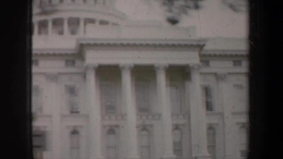 A soft 1957 San Francisco 8mm view of a white neoclassical facade with columns, upper windows, and dark frame-edge shadows.