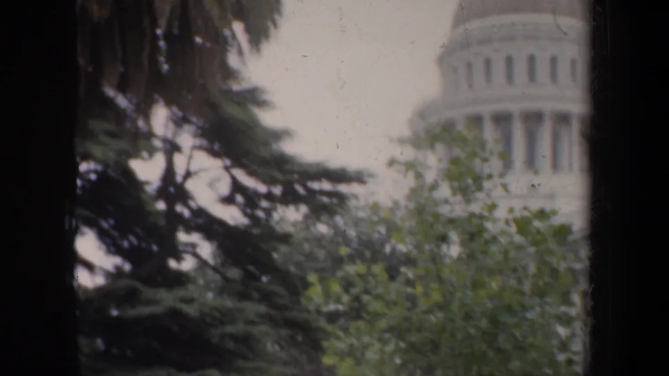 1957 8mm frame with the capitol-style dome cropped at the right, surrounded by trees and dark vertical foreground framing.