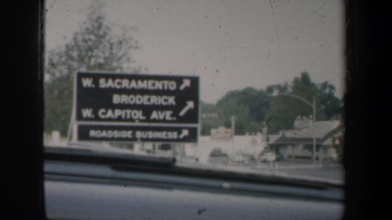 1957 California car-window view of a roadside directional sign listing W. Sacramento, Broderick, W. Capitol Ave., and roadside businesses.