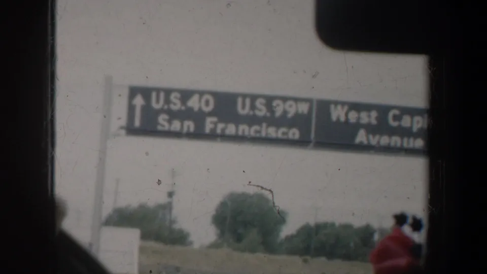 1957 California car-window view of an overhead highway sign pointing to U.S. 40, U.S. 99W, San Francisco, and West Capitol Avenue.