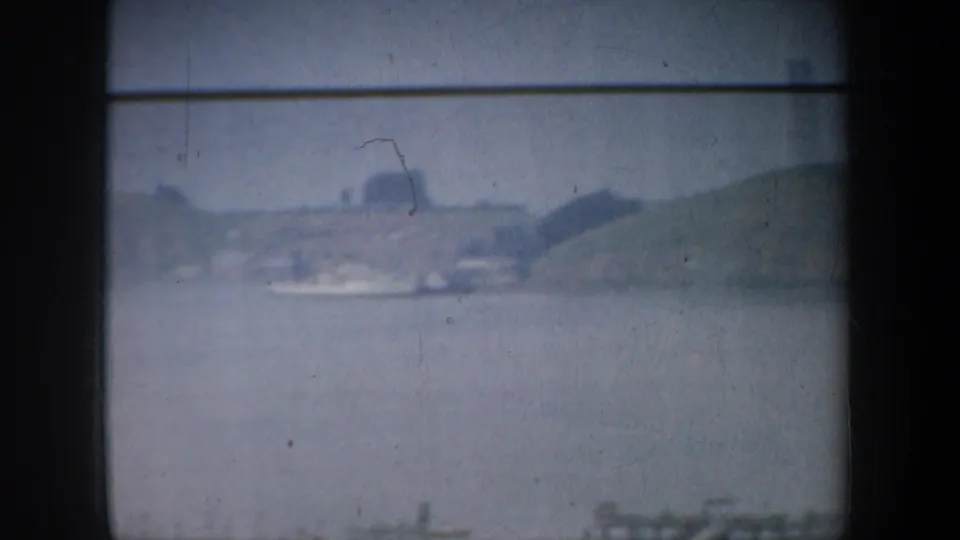 Hazy 1957 Bay Area waterfront view with water, distant shoreline, low hills, and a bridge structure partly obscured by film softness.