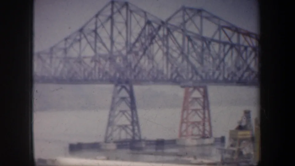 1957 San Francisco-area view of a large steel truss bridge over water, with industrial structures visible near the shore.