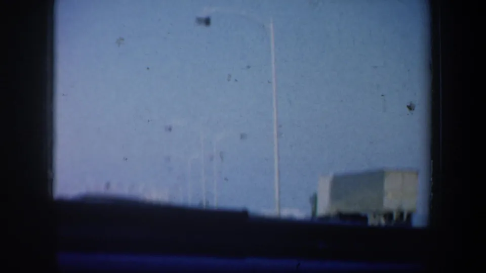 1957 San Francisco home-movie street cutaway with a lamppost, distant structures, and dark vehicle-window framing.