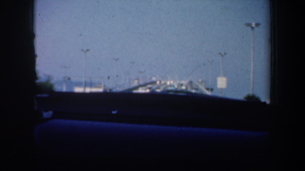 View through a car windshield toward traffic and bridge lights under a blue sky.