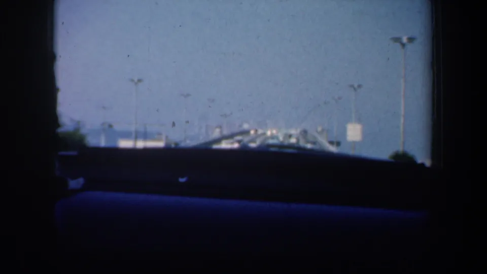 1957 San Francisco car-window view with dashboard silhouette, distant traffic, bridge lights and sky ahead.