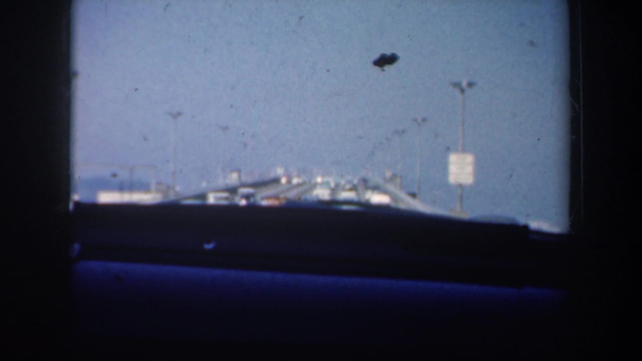 Windshield view with dashboard edge, bridge lights, distant cars and a roadside sign.