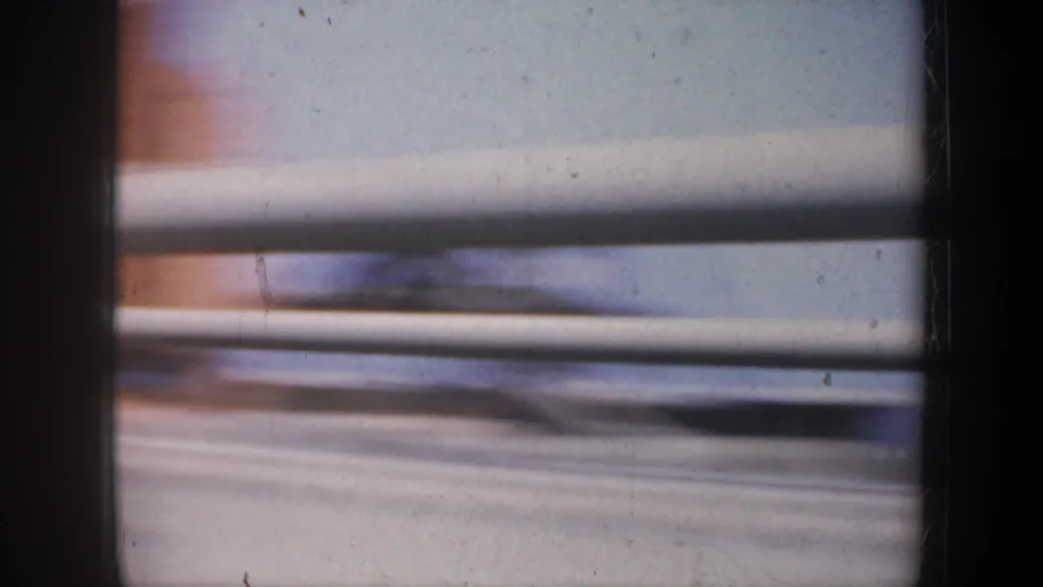 1957 San Francisco moving-car view with bridge railings, motion blur and a pale expanse of water or shoreline beyond.