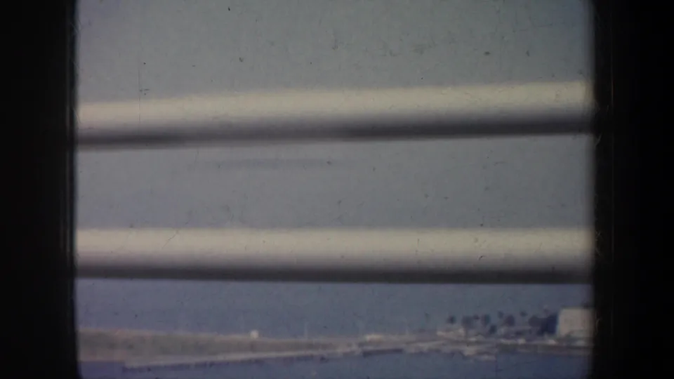 San Francisco Bay shoreline in 1957 appears beyond horizontal slats, with low buildings and hazy blue water.